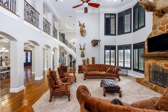 living room featuring dark hardwood / wood-style floors, ceiling fan with notable chandelier, a fireplace, a towering ceiling, and ornamental molding