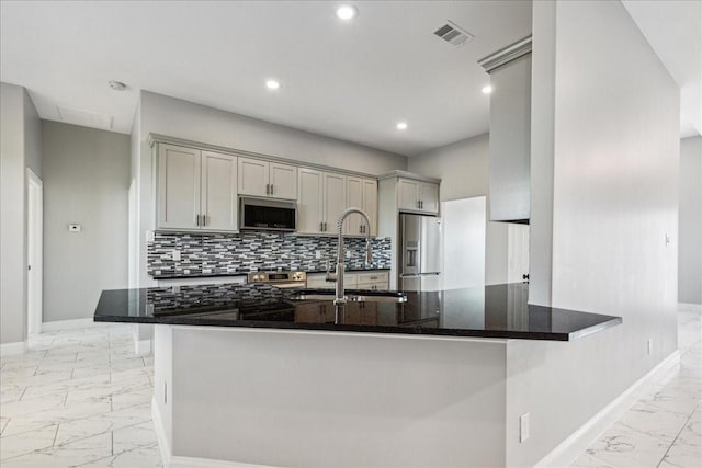 kitchen with stainless steel appliances, dark stone counters, sink, backsplash, and gray cabinetry