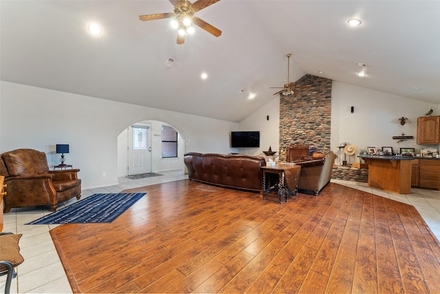 living room featuring arched walkways, high vaulted ceiling, light wood finished floors, and a ceiling fan