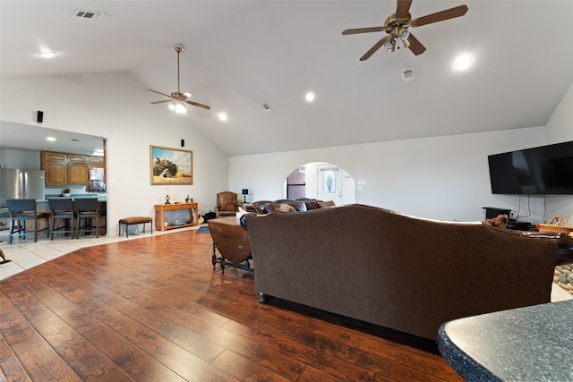 living room featuring arched walkways, high vaulted ceiling, light wood-type flooring, and visible vents