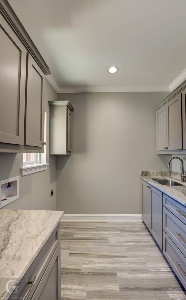 kitchen with gray cabinets, ornamental molding, light stone countertops, and sink