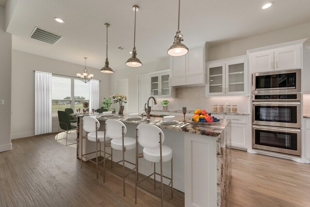 kitchen featuring stainless steel appliances, a kitchen island with sink, white cabinets, and hanging light fixtures