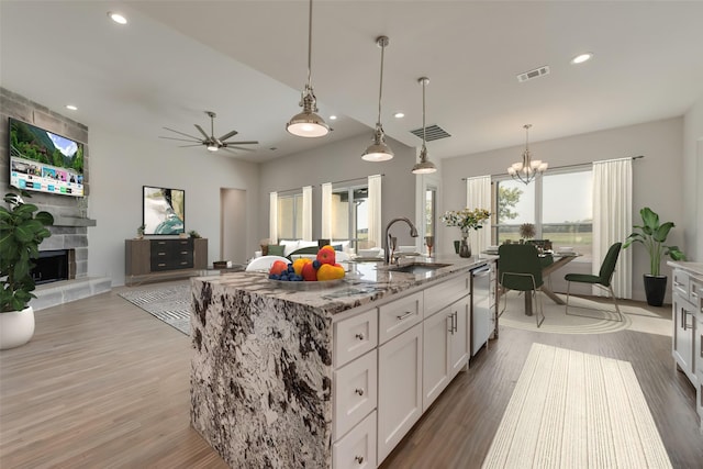 kitchen with a center island with sink, light stone countertops, a fireplace, white cabinets, and ceiling fan with notable chandelier