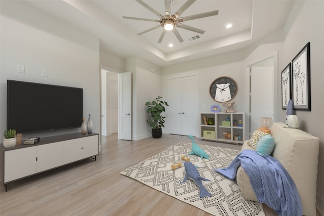 living room with a raised ceiling, ceiling fan, and light hardwood / wood-style floors