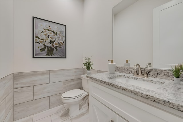 bathroom featuring toilet, tile patterned floors, tile walls, and vanity