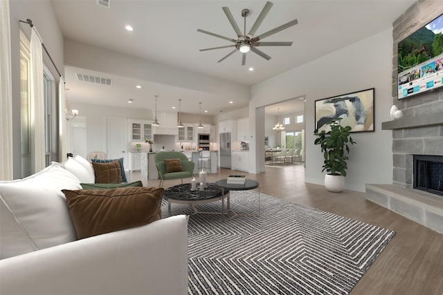 living room featuring ceiling fan with notable chandelier, hardwood / wood-style floors, and a fireplace