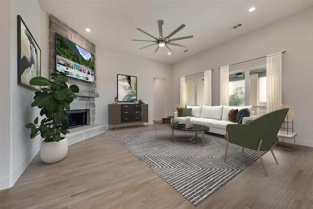 living room with a tile fireplace, light wood-type flooring, and ceiling fan