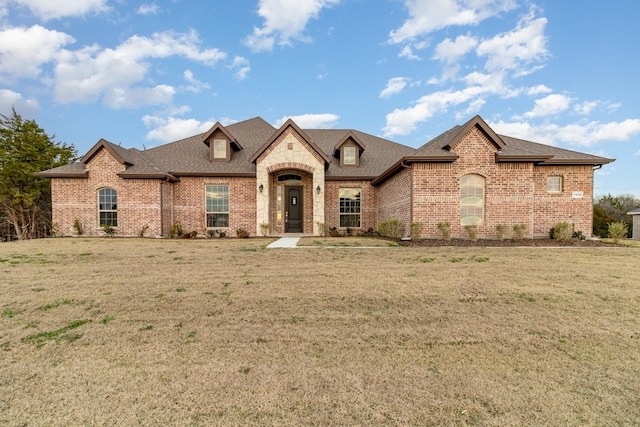 french country home with brick siding, a front lawn, and roof with shingles