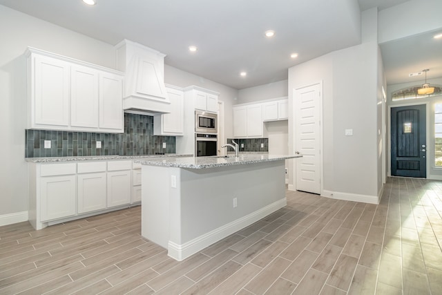 kitchen with decorative backsplash, an island with sink, appliances with stainless steel finishes, and white cabinets