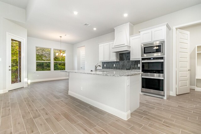 kitchen featuring white cabinetry, custom range hood, backsplash, light stone countertops, and appliances with stainless steel finishes