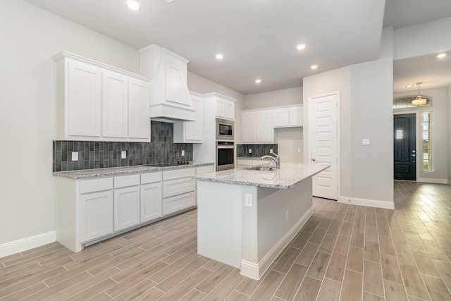 kitchen with white cabinetry, decorative backsplash, an island with sink, sink, and appliances with stainless steel finishes