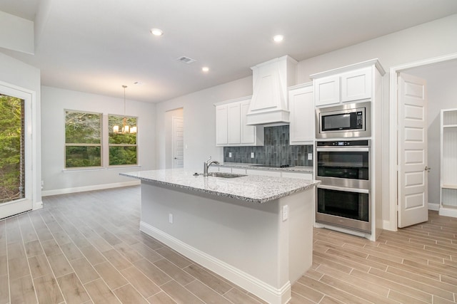 kitchen featuring premium range hood, appliances with stainless steel finishes, an island with sink, and white cabinetry