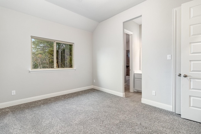 unfurnished bedroom featuring light carpet, ensuite bath, baseboards, and vaulted ceiling