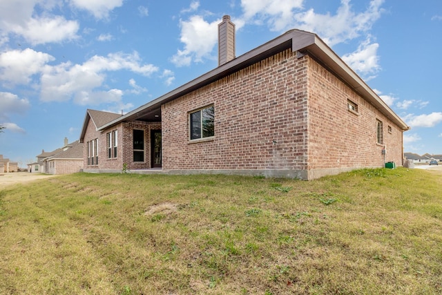 view of property exterior with brick siding, a yard, and a chimney