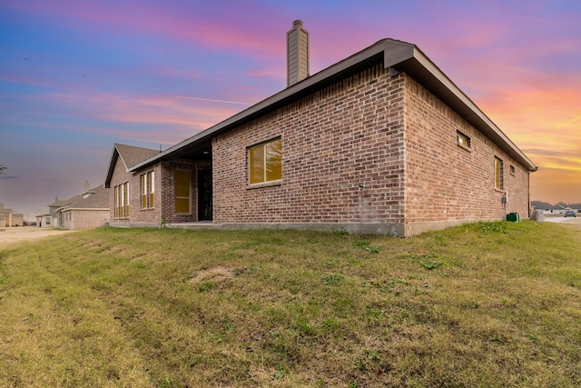 property exterior at dusk with brick siding, a lawn, and a chimney