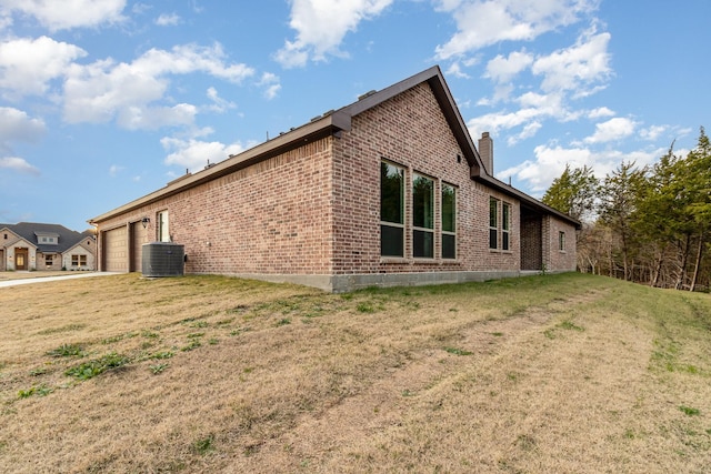 view of side of home with central air condition unit, a garage, brick siding, a yard, and a chimney