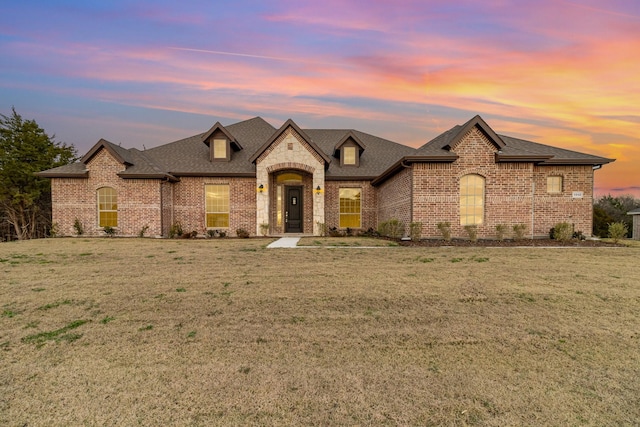 french country style house featuring brick siding, a lawn, and a shingled roof