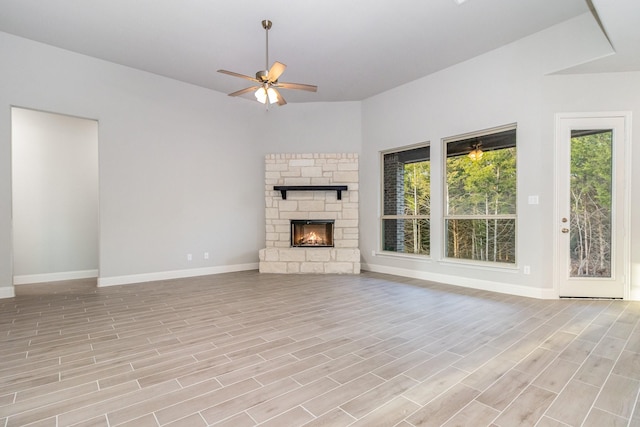 unfurnished living room with a ceiling fan, light wood-style floors, a stone fireplace, and baseboards