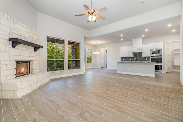 unfurnished living room featuring sink, a fireplace, ceiling fan with notable chandelier, and light hardwood / wood-style floors