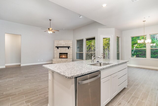 kitchen featuring stainless steel dishwasher, ceiling fan with notable chandelier, white cabinets, sink, and a stone fireplace