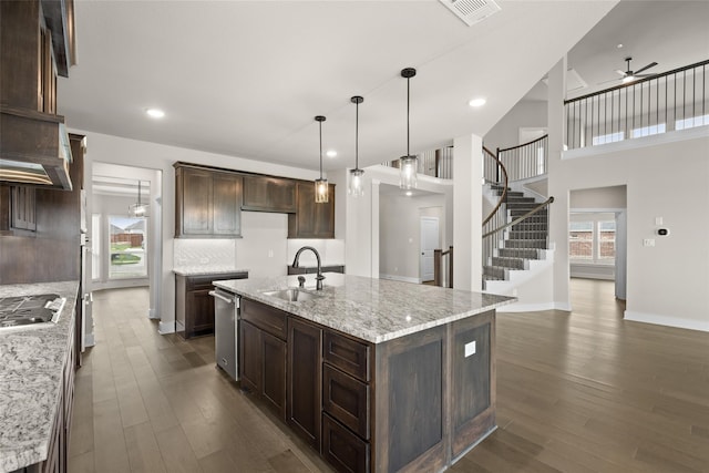 kitchen featuring dark hardwood / wood-style floors, ceiling fan, decorative light fixtures, light stone counters, and a kitchen island with sink