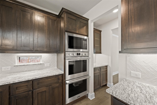 kitchen featuring light stone counters, dark hardwood / wood-style flooring, stainless steel appliances, tasteful backsplash, and dark brown cabinets