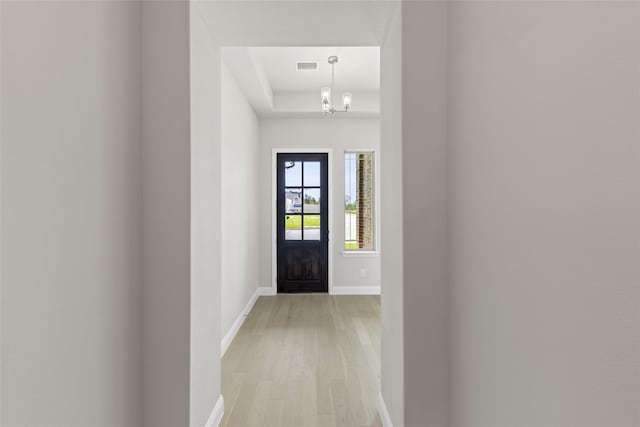 hall featuring light hardwood / wood-style floors, a raised ceiling, and an inviting chandelier