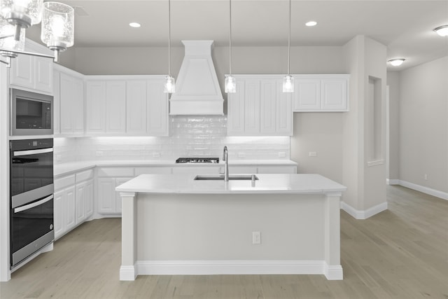 kitchen with white cabinets, light countertops, a sink, and a center island with sink