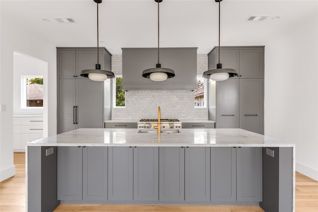 kitchen with decorative light fixtures, decorative backsplash, light wood-type flooring, a large island, and light stone countertops