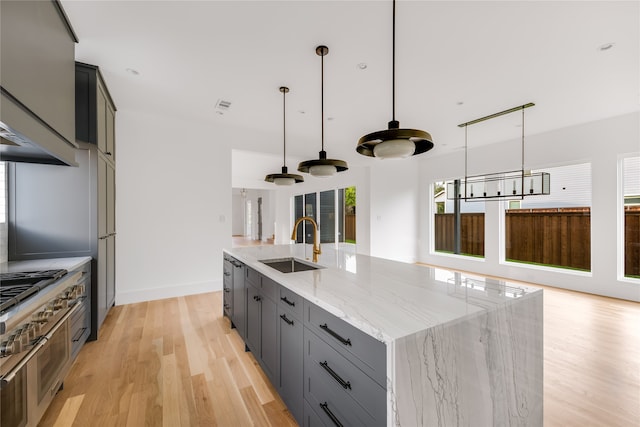 kitchen featuring light wood-type flooring, decorative light fixtures, light stone counters, and a center island with sink