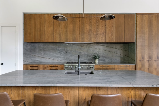 kitchen with a breakfast bar, sink, pendant lighting, and light stone counters