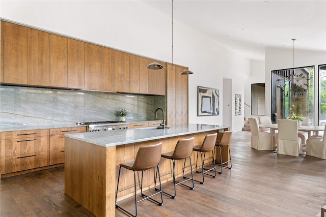 kitchen with hanging light fixtures, decorative backsplash, an island with sink, high vaulted ceiling, and hardwood / wood-style flooring