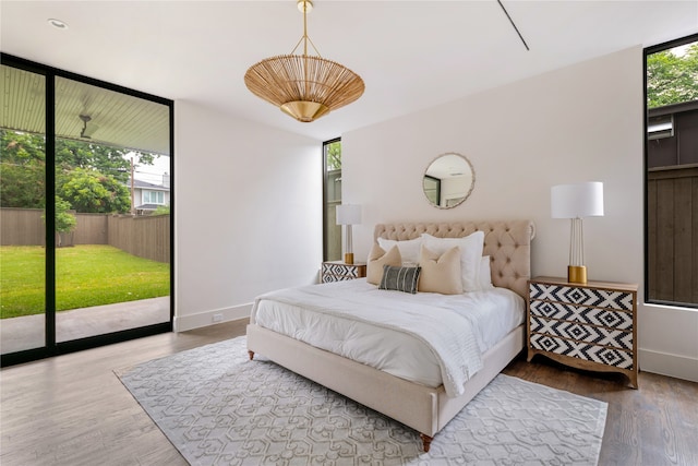 bedroom featuring a wall of windows, multiple windows, hardwood / wood-style flooring, and access to exterior