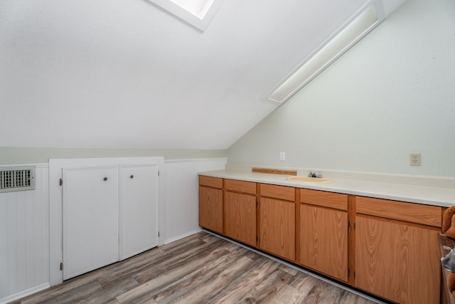 interior space featuring lofted ceiling with skylight and light hardwood / wood-style flooring