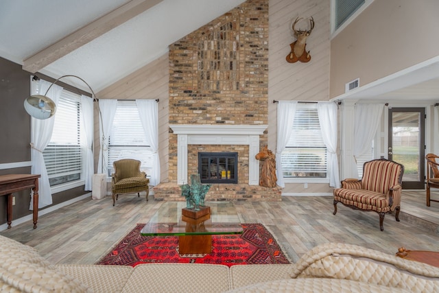 living room with beam ceiling, wood-type flooring, a brick fireplace, wooden walls, and high vaulted ceiling