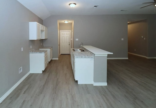 kitchen with sink, white cabinets, vaulted ceiling, and light hardwood / wood-style flooring