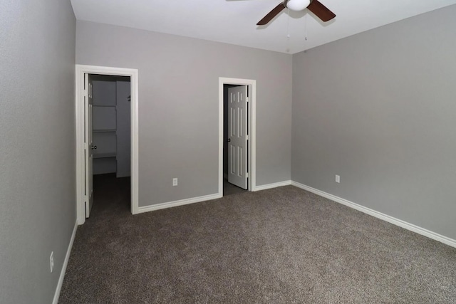 unfurnished bedroom featuring dark colored carpet, a walk in closet, a closet, and ceiling fan