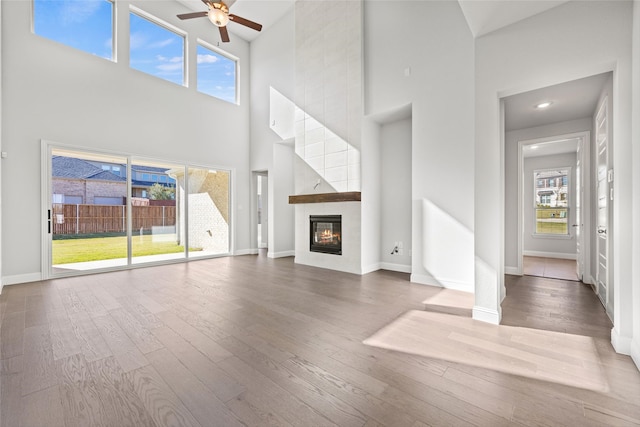 unfurnished living room featuring hardwood / wood-style floors, ceiling fan, a fireplace, and a high ceiling