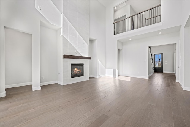 unfurnished living room featuring a tile fireplace, a high ceiling, and hardwood / wood-style flooring