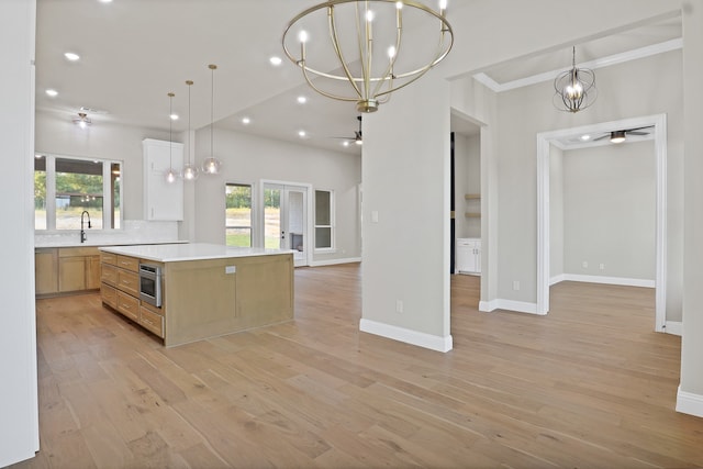 kitchen featuring light wood-type flooring, sink, crown molding, hanging light fixtures, and a spacious island