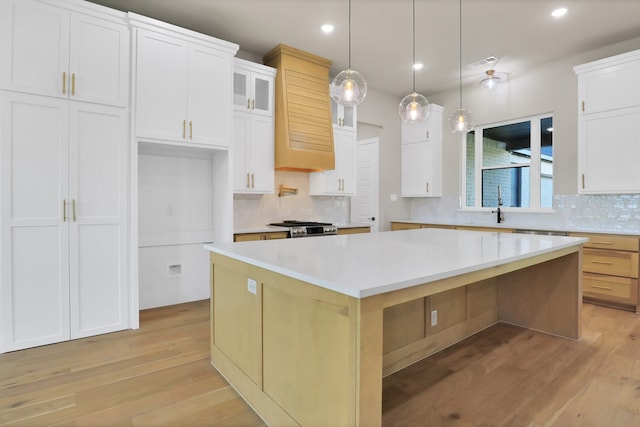 kitchen featuring hanging light fixtures, light hardwood / wood-style floors, white cabinets, and a spacious island