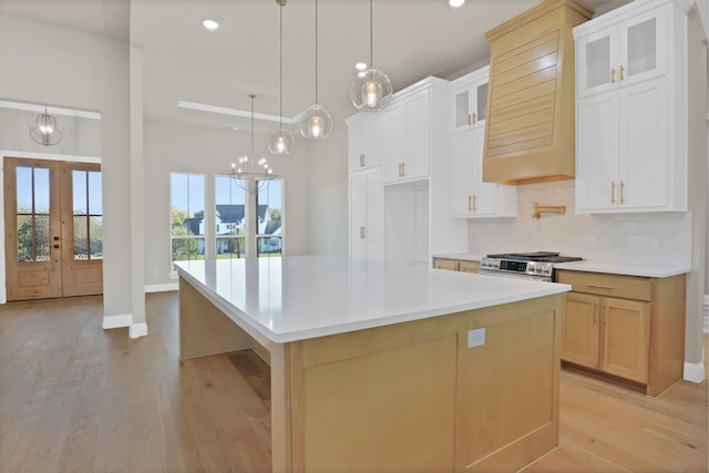 kitchen with premium range hood, a large island, white cabinetry, stainless steel gas range oven, and light hardwood / wood-style floors