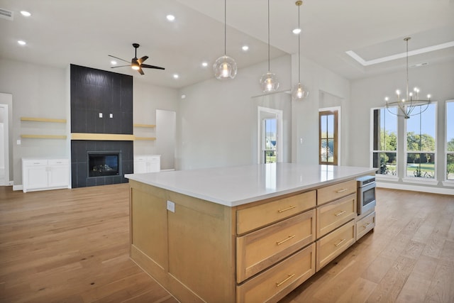 kitchen featuring light brown cabinets, a tiled fireplace, stainless steel oven, a spacious island, and light wood-type flooring