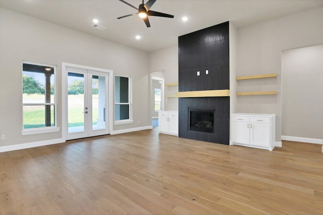 unfurnished living room with a fireplace, french doors, light wood-type flooring, and ceiling fan