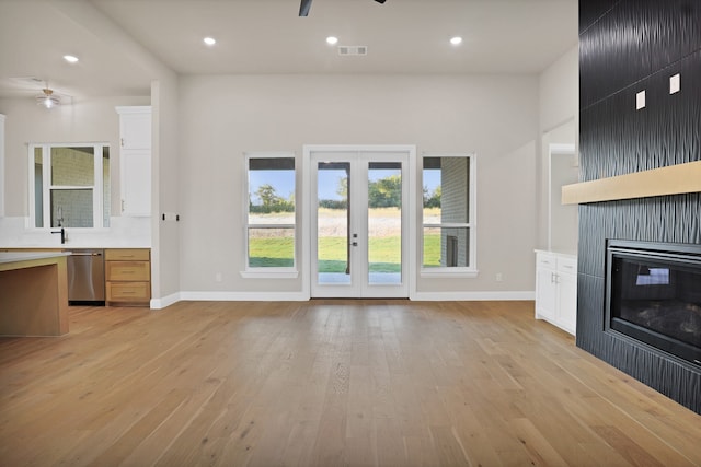 unfurnished living room with ceiling fan, a fireplace, light wood-type flooring, and french doors