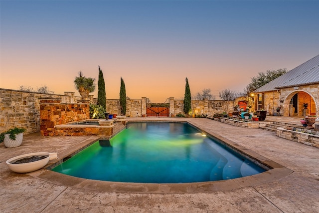 pool at dusk with an in ground hot tub and a patio