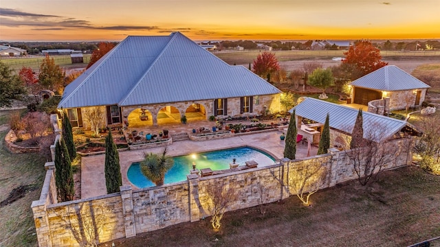 pool at dusk featuring a patio area and an outbuilding