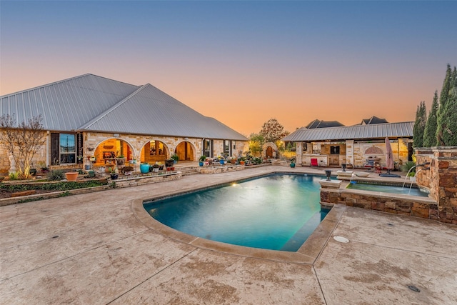 pool at dusk featuring pool water feature, a patio area, and an in ground hot tub