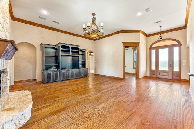 unfurnished living room with hardwood / wood-style floors, ornamental molding, a notable chandelier, and a stone fireplace