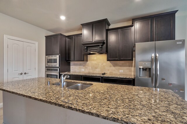 kitchen with backsplash, sink, dark stone countertops, dark brown cabinets, and stainless steel appliances